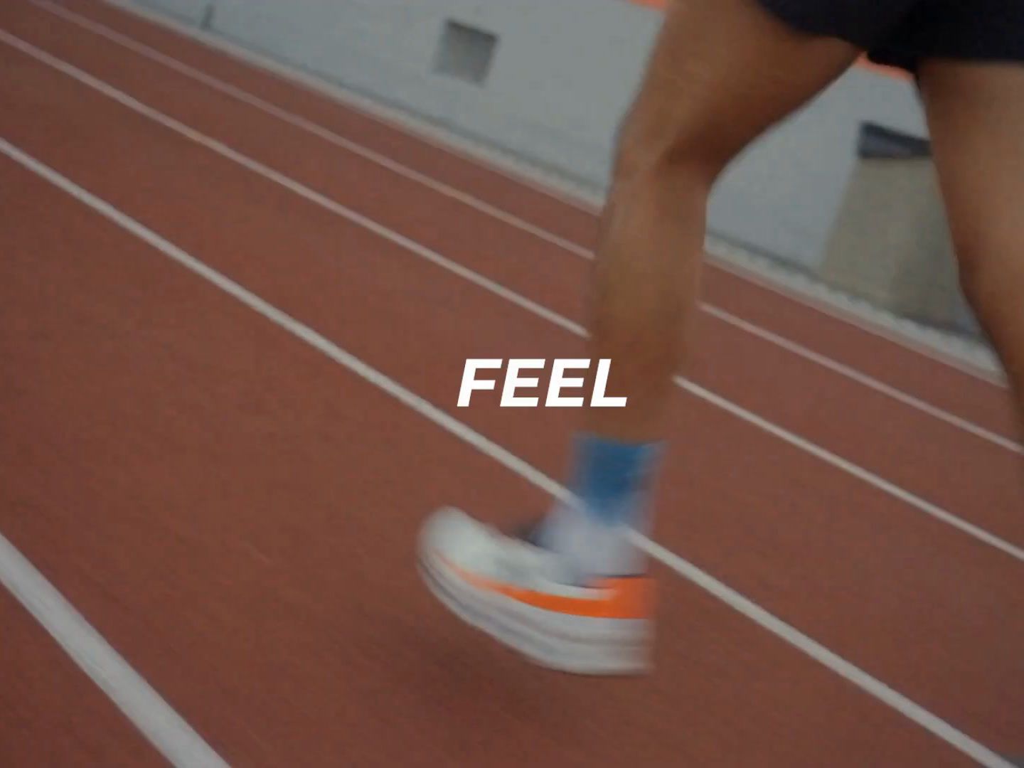 Close-up of a runner's shoes on a red track with the word FEEL, from the activewear campaign video.
